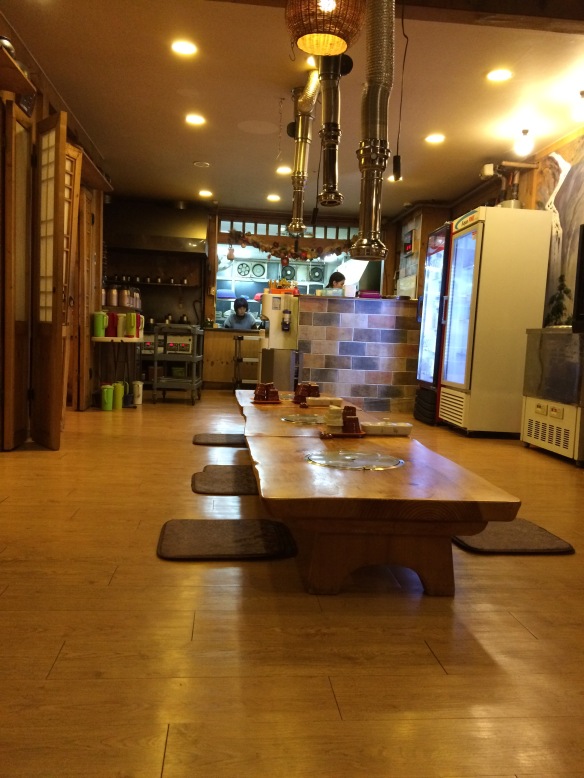 Traditional Korean restaurant. Note the flat metal disks in center of table. These are covers for the unused woks. Servers bring a pail of coals to place under wok to heat the pan for food preparation.